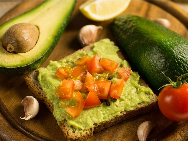 A slice of bread with avocado, tomatoes, and garlic.