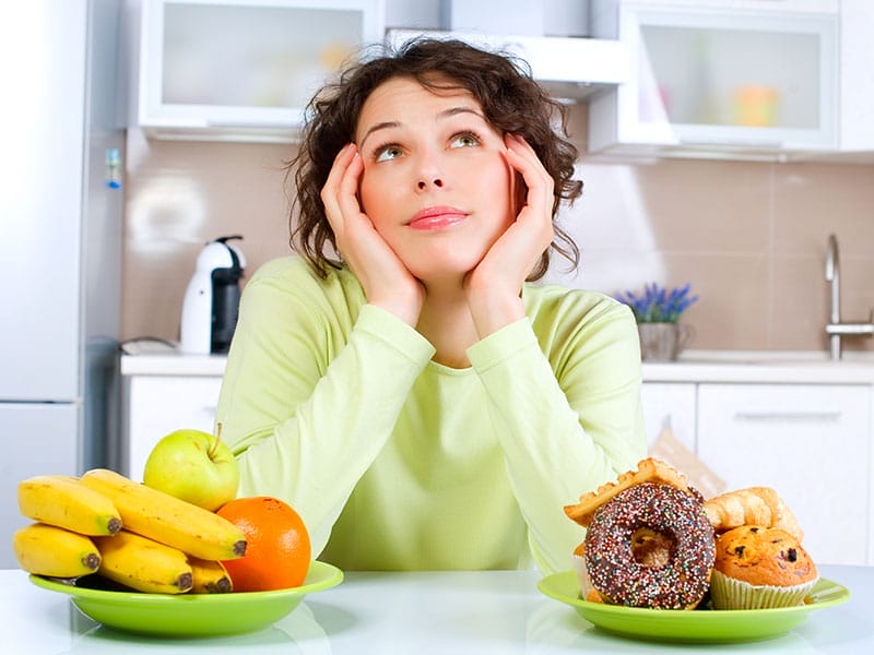 A woman looking at a plate of fruit and donuts.