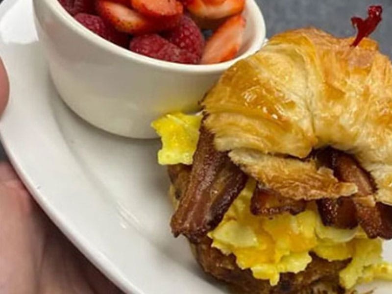 A loaded croissant sandwich with bacon, eggs and strawberries.